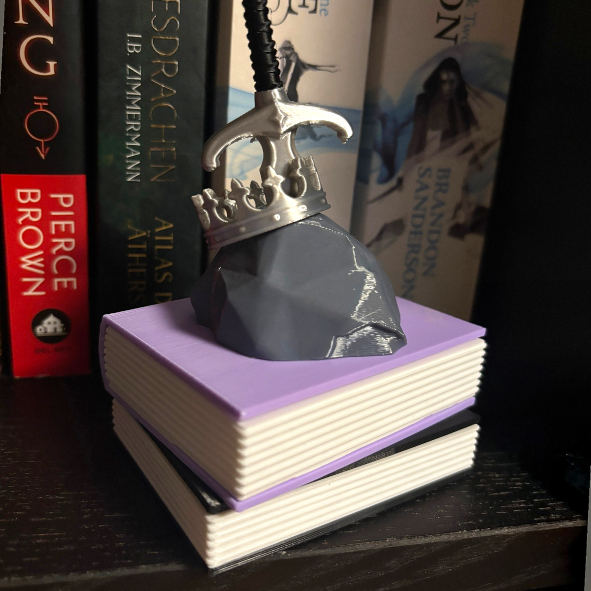 Verleihe deinem Bücherregal, deinem Schlüsselbund oder deinem Weihnachtsbaum den perfekten Fantasy-Vibe! Dieses liebevoll gestaltete "Fantasy" Book Pile mit Krone, Schwert- und Stein-Details ist ein absoluter Hingucker für alle Buchliebhaber.