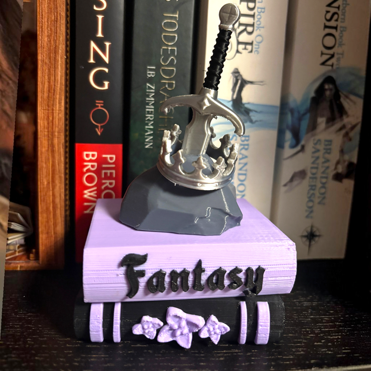 Verleihe deinem Bücherregal, deinem Schlüsselbund oder deinem Weihnachtsbaum den perfekten Fantasy-Vibe! Dieses liebevoll gestaltete "Fantasy" Book Pile mit Krone, Schwert- und Stein-Details ist ein absoluter Hingucker für alle Buchliebhaber.