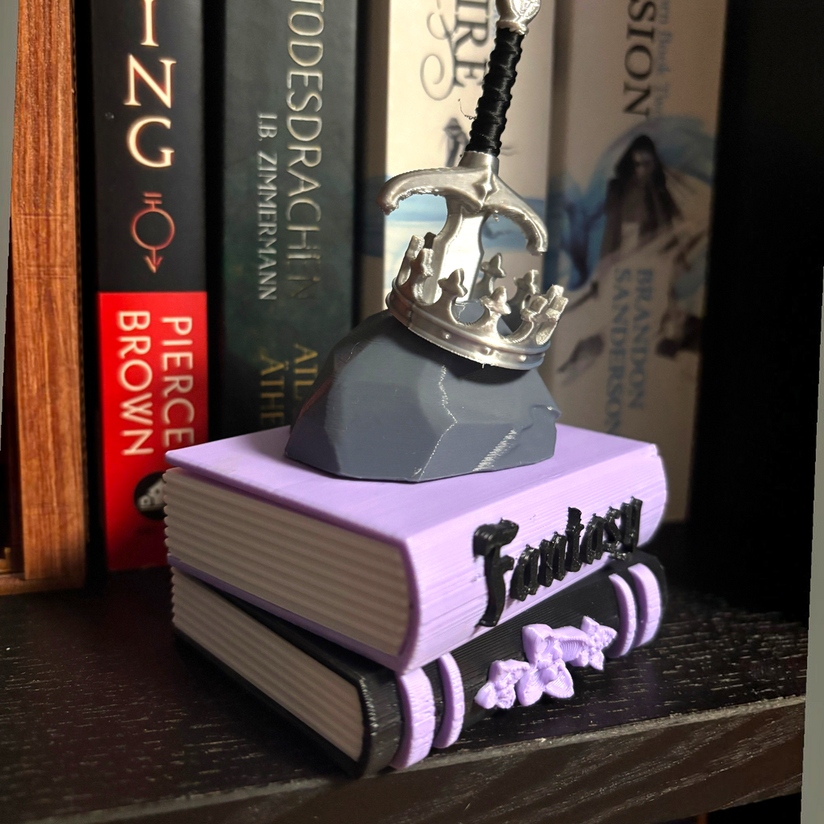Verleihe deinem Bücherregal, deinem Schlüsselbund oder deinem Weihnachtsbaum den perfekten Fantasy-Vibe! Dieses liebevoll gestaltete "Fantasy" Book Pile mit Krone, Schwert- und Stein-Details ist ein absoluter Hingucker für alle Buchliebhaber.