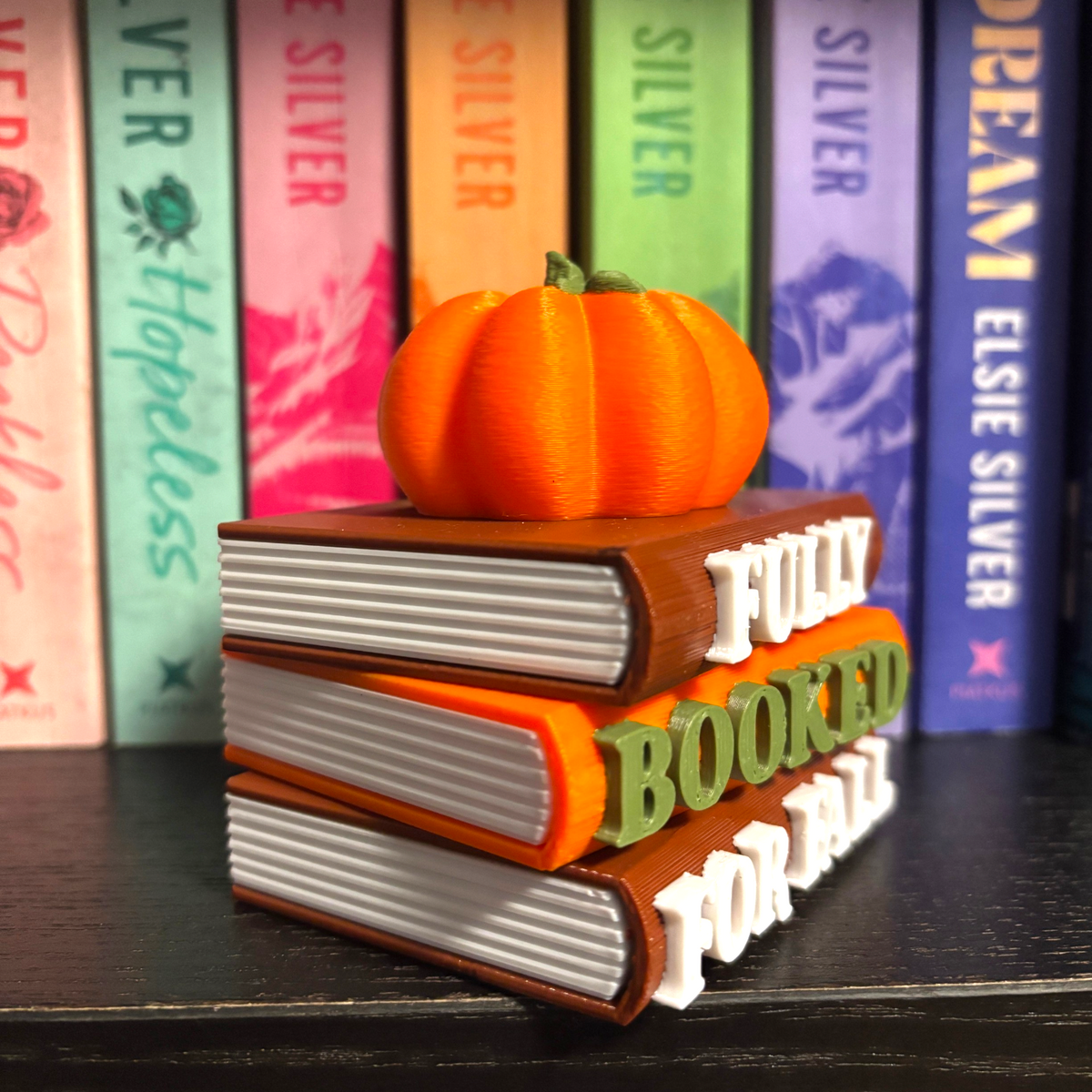 Verleihe deinem Bücherregal, deinem Schlüsselbund oder deinem Weihnachtsbaum den perfekten Herbst-Vibe! Dieses liebevoll gestaltete "Fully Booked for Fall" Book Pile mit Kürbis-Details ist ein absoluter Hingucker für alle Buchliebhaber.