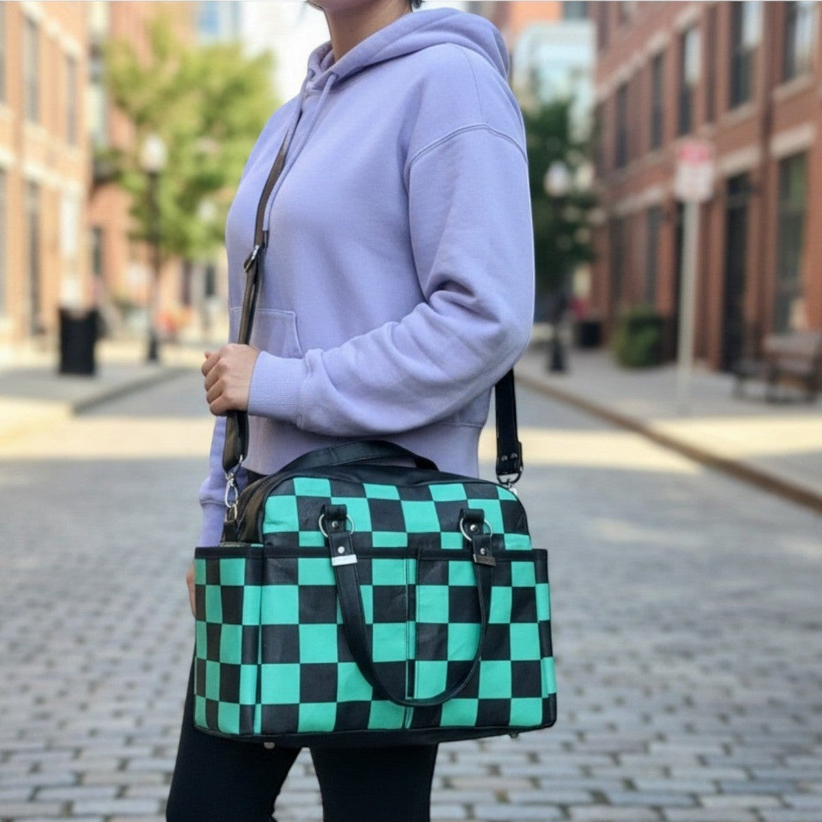 Schneckenschmiede Belle Baby Windeltasche mit grün-schwarzem Karomuster, Kunstlederdetails und praktischem Umhängegurt.