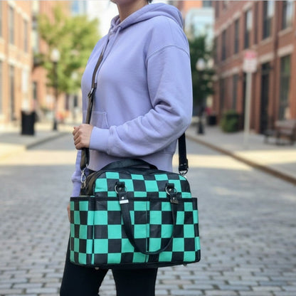 Schneckenschmiede Belle Baby Windeltasche mit grün-schwarzem Karomuster, Kunstlederdetails und praktischem Umhängegurt.