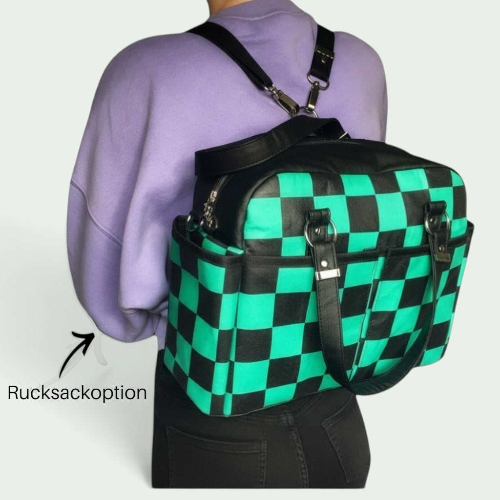Schneckenschmiede Belle Baby Windeltasche mit grün-schwarzem Karomuster, als Rucksack getragen mit Kunstlederdetails