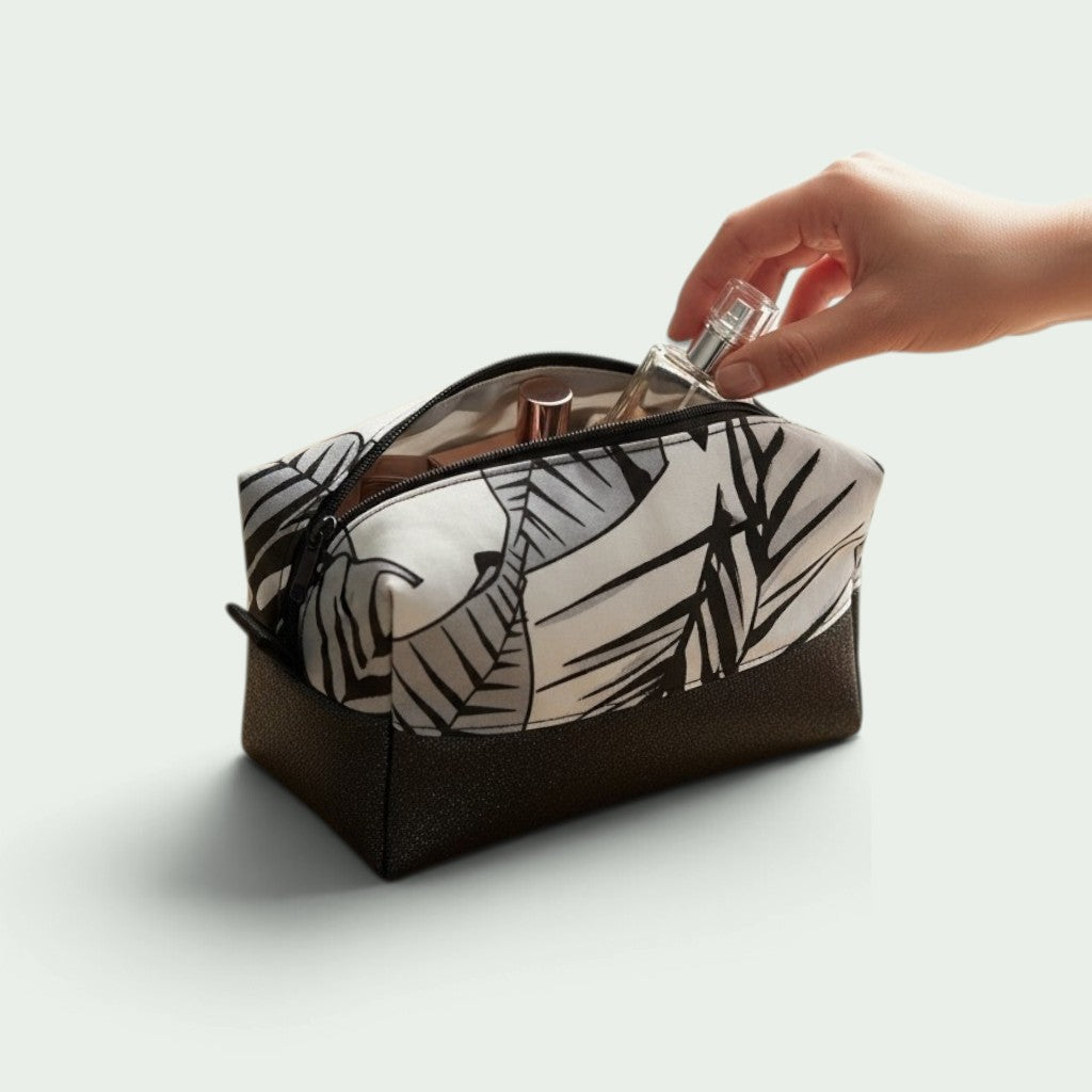 Schneckenschmiede Boxy Bag Kosmetiktasche mit schwarz-weißem Blattmuster und braunem Boden, Hand greift nach Parfüm