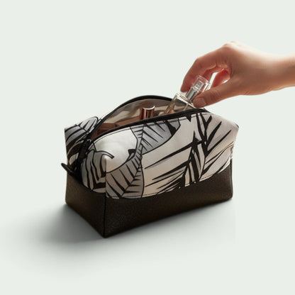Schneckenschmiede Boxy Bag Kosmetiktasche mit schwarz-weißem Blattmuster und braunem Boden, Hand greift nach Parfüm