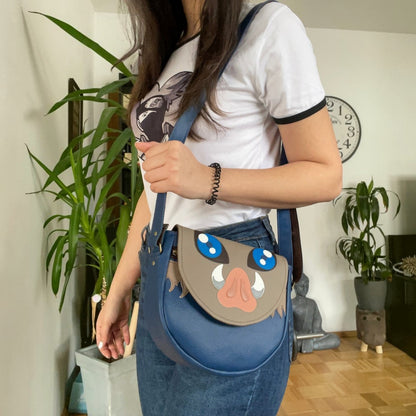 Schneckenschmiede Umhängetasche aus blauem Kunstleder mit Inosuke-Masken-Applikation, getragen von einer Frau.