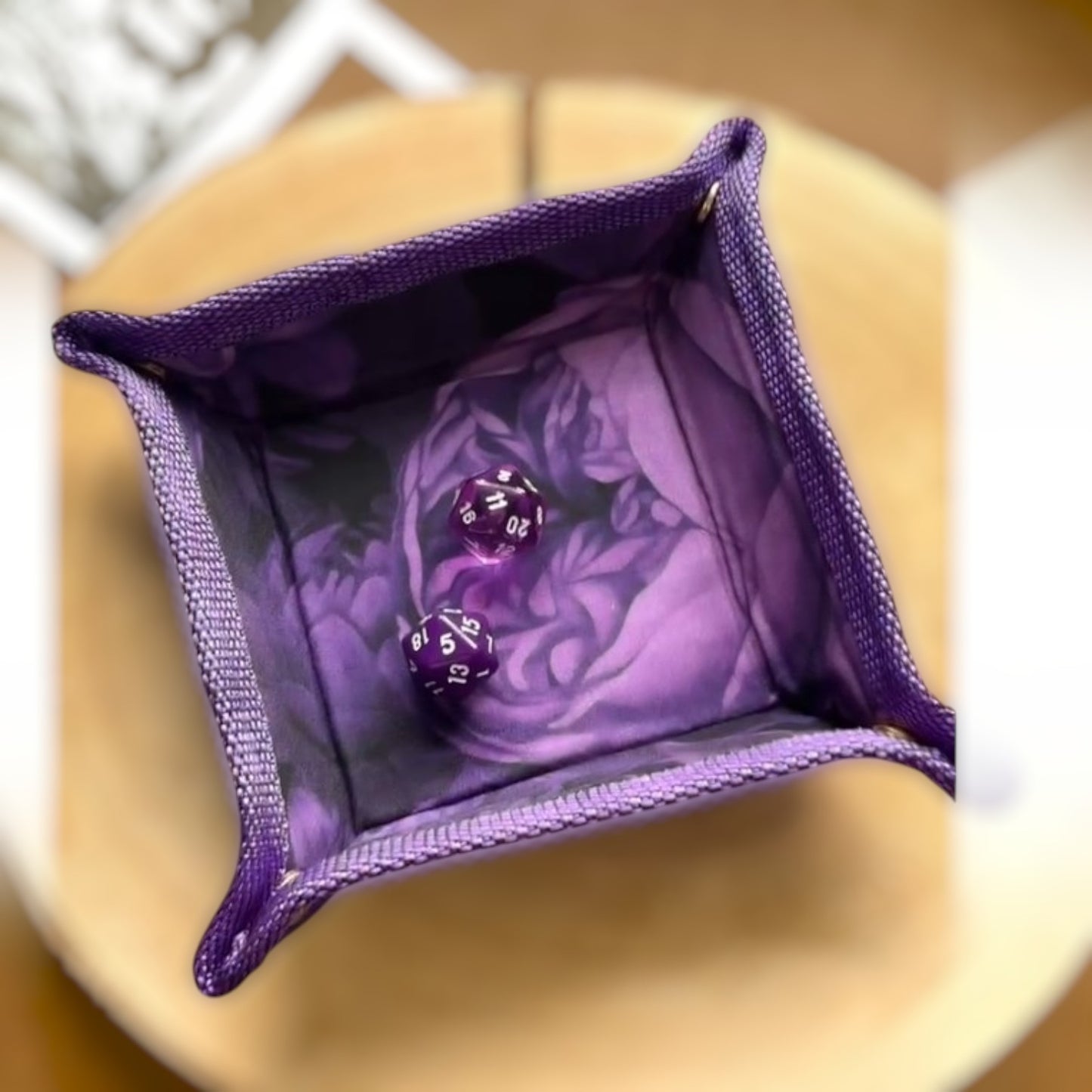Schneckenschmiede faltbares lila Würfeltablett mit Blumenmuster und zwei lila W20 Würfeln auf einer Holzscheibe