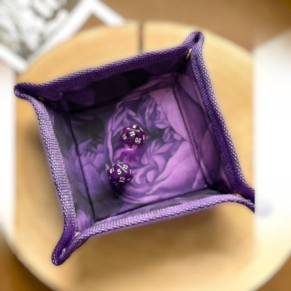 Schneckenschmiede faltbares lila Würfeltablett mit Blumenmuster und zwei lila W20 Würfeln auf einer Holzscheibe