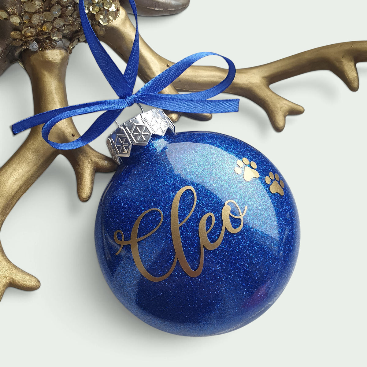 Schneckenschmiede personalisierte blaue Weihnachtsbaumkugel mit Glitzer, goldenem Namen Cleo und Pfotenabdruck-Motiv