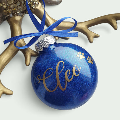 Schneckenschmiede personalisierte blaue Weihnachtsbaumkugel mit Glitzer, goldenem Namen Cleo und Pfotenabdruck-Motiv