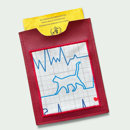 Schneckenschmiede Impfpasshülle aus rotem Kunstleder mit aufgesticktem EKG-Katzenmotiv und gelbem Impfpass