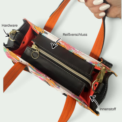 Schneckenschmiede Transponster Umhängetasche mit Reißverschlussfach, orangefarbenen Henkeln und buntem Print-Design.