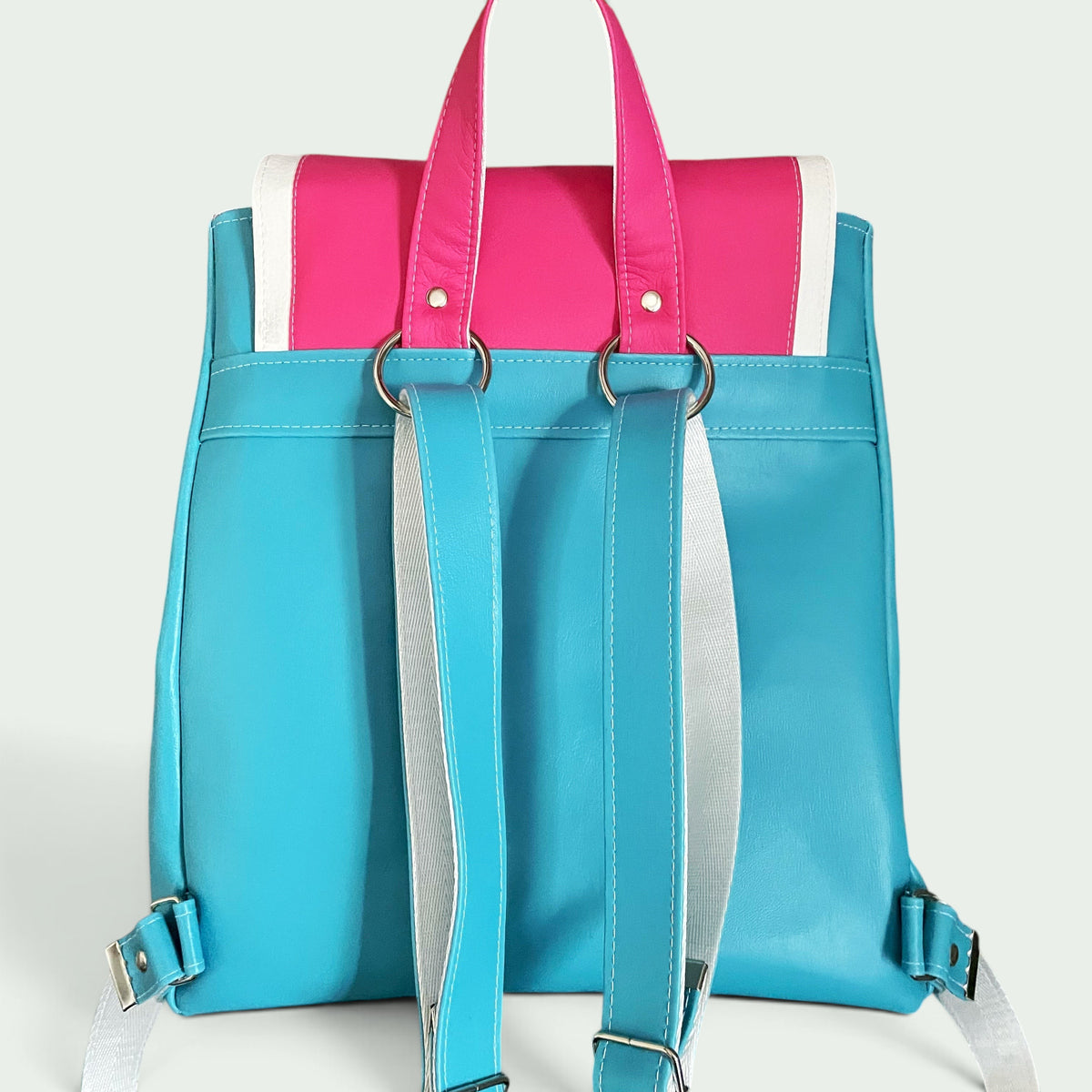 Schneckenschmiede Rucksack in Türkis, Pink und Weiß aus Kunstleder mit verstellbaren Trägern vor einer Ziegelwand
