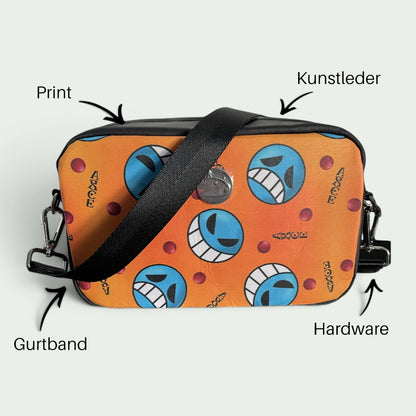 Schneckenschmiede Umhängetasche Catalina mit orangefarbenem Anime-Print, schwarzem Gurtband und Kunstleder-Details.