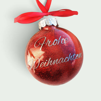 Schneckenschmiede Weihnachtsornament aus rotem Glitzerkunststoff mit Frohe Weihnachten Schriftzug und roter Schleife