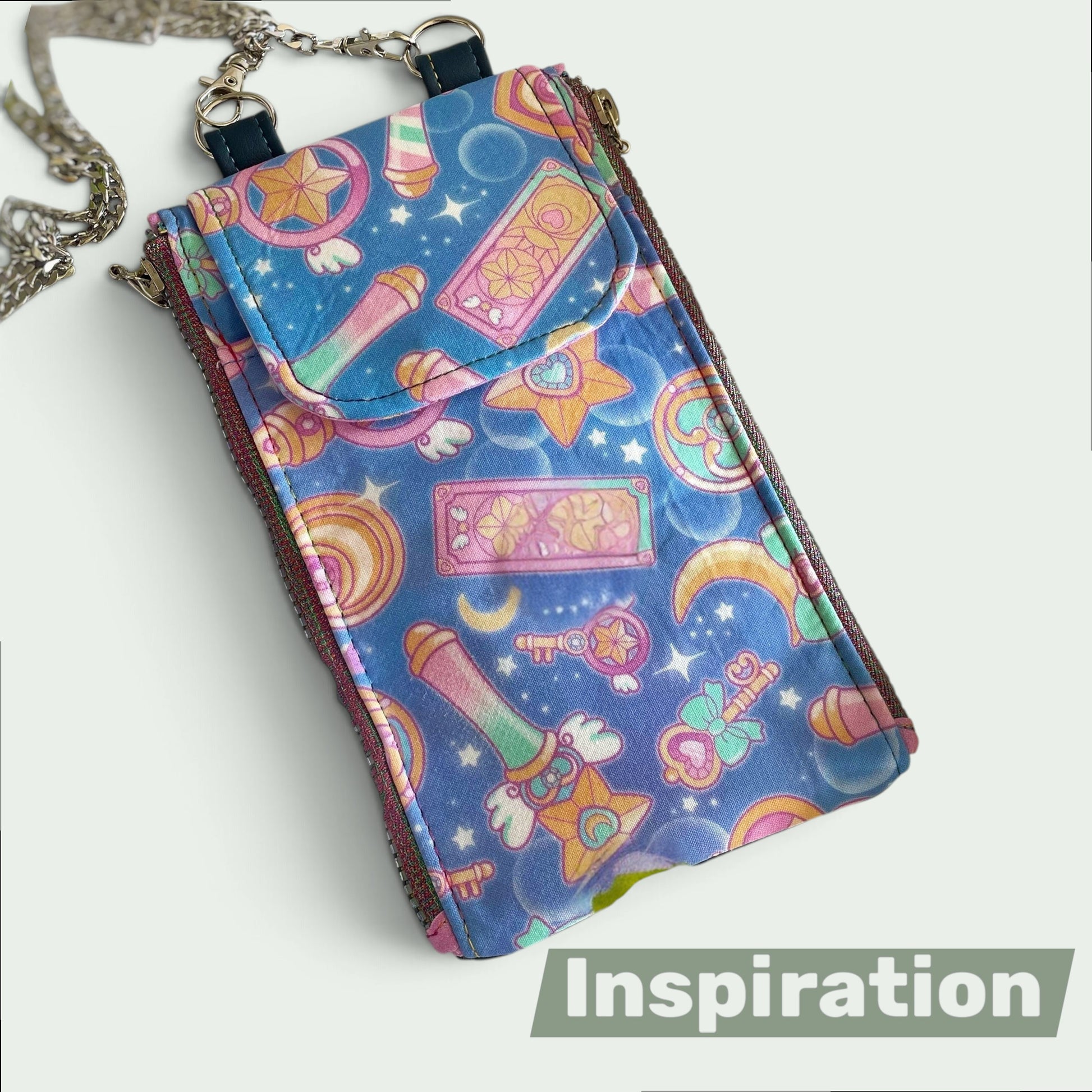 Schneckenschmiede Zip n Go Handytasche mit buntem Anime-Muster, Kartenfächern und silberner Kette als Umhängetasche.